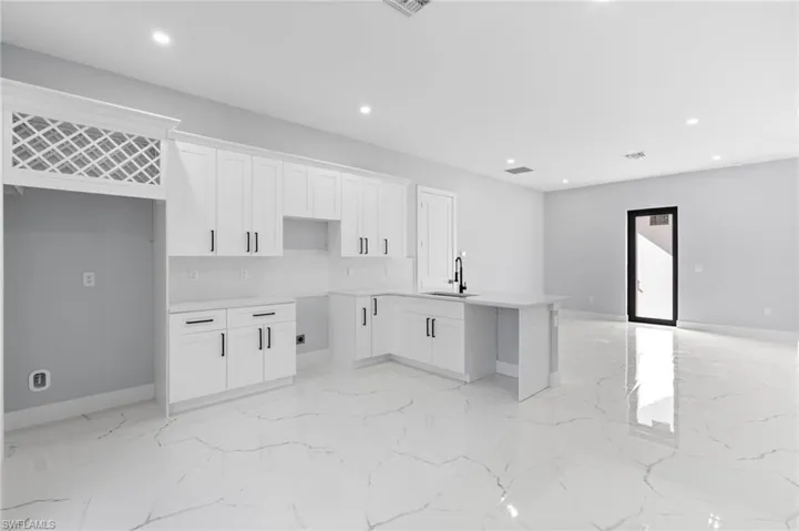 Kitchen featuring white cabinets, a peninsula, recessed lighting, light stone countertops, and light marble finish floors