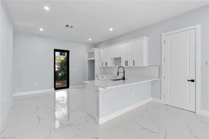 Kitchen with white cabinets, a peninsula, light stone countertops, recessed lighting, and light marble finish flooring