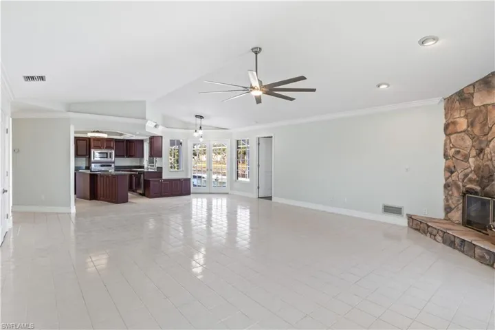 Tiled living room with ceiling fan, a stone fireplace, crown molding, and vaulted ceiling