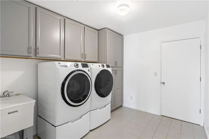Laundry area featuring light tile patterned flooring, cabinets, sink, and washing machine and clothes dryer