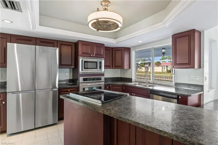 Kitchen featuring a raised ceiling, sink, dark stone countertops, light tile patterned floors, and appliances with stainless steel finishes