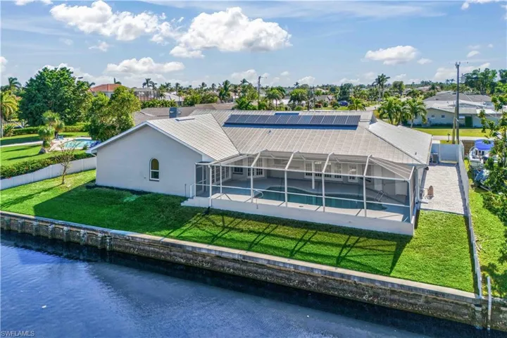 Rear view of property featuring solar panels, a yard, a water view, and a lanai