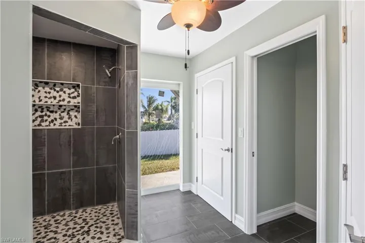 Bathroom featuring tiled shower, tile patterned flooring, and ceiling fan