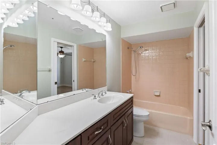 Full bathroom with vanity, tile patterned floors, tiled shower / bath combo, ceiling fan, and toilet