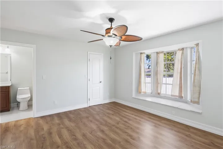 Unfurnished bedroom with ceiling fan, wood-type flooring, and connected bathroom