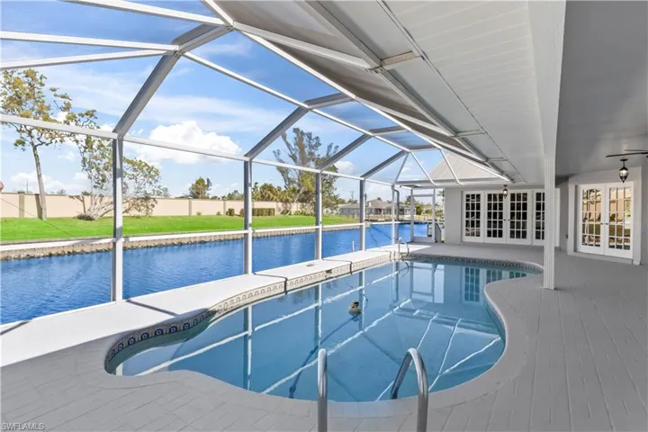 View of swimming pool with french doors, a water view, a patio area, and a lanai
