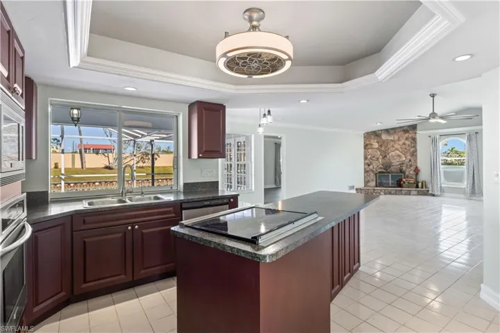 Kitchen with a raised ceiling, sink, ceiling fan, a fireplace, and appliances with stainless steel finishes