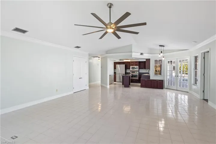 Unfurnished living room with french doors, ornamental molding, ceiling fan, light tile patterned floors, and lofted ceiling