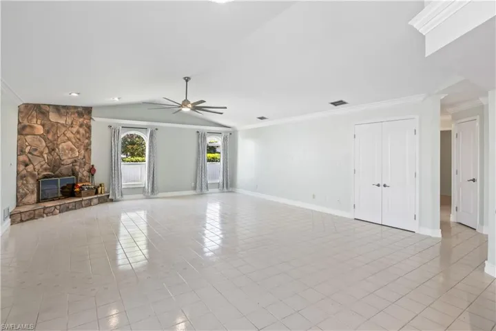 Unfurnished living room with ornamental molding, vaulted ceiling, ceiling fan, light tile patterned floors, and a fireplace