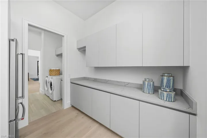 Kitchen with light stone counters, white cabinets, washer and clothes dryer, and light wood finished floors