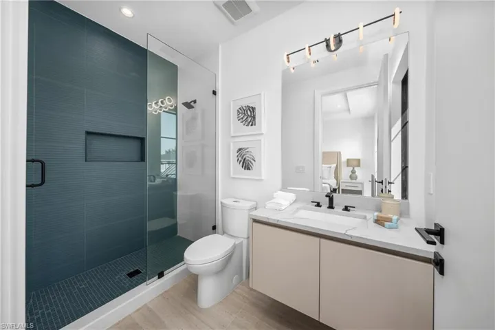 Ensuite bathroom featuring visible vents, toilet, a stall shower, vanity, and ensuite bath