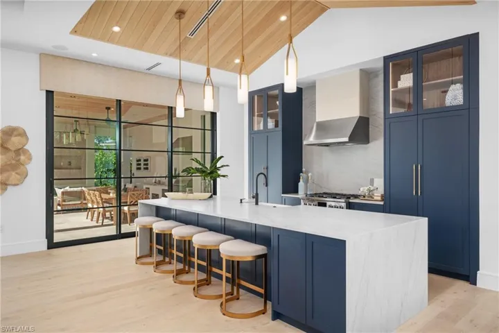 Kitchen featuring hanging light fixtures, blue cabinetry, wall chimney exhaust hood, and glass insert cabinets