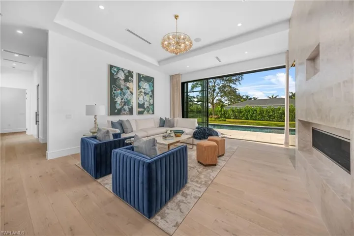Living room with light wood finished floors, baseboards, a raised ceiling, an inviting chandelier, and a high end fireplace