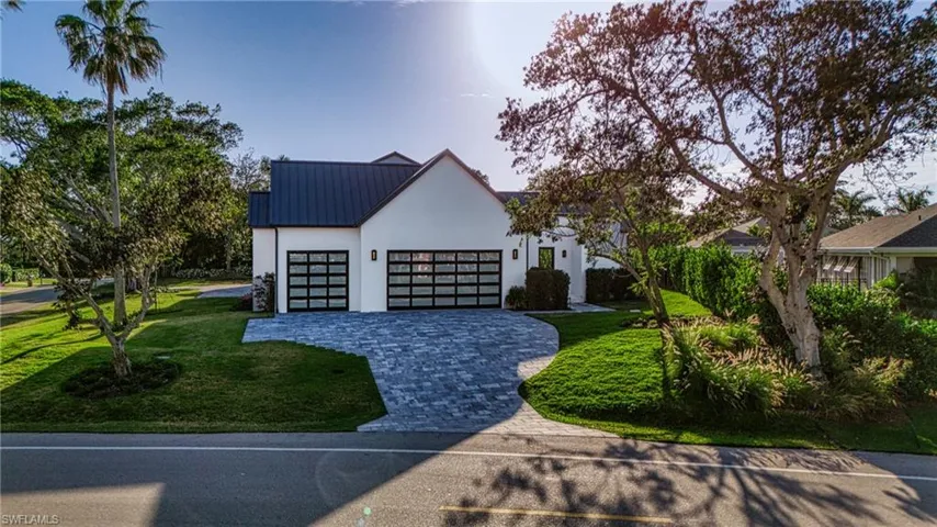 Modern farmhouse featuring decorative driveway, stucco siding, an attached garage, metal roof, and a front lawn