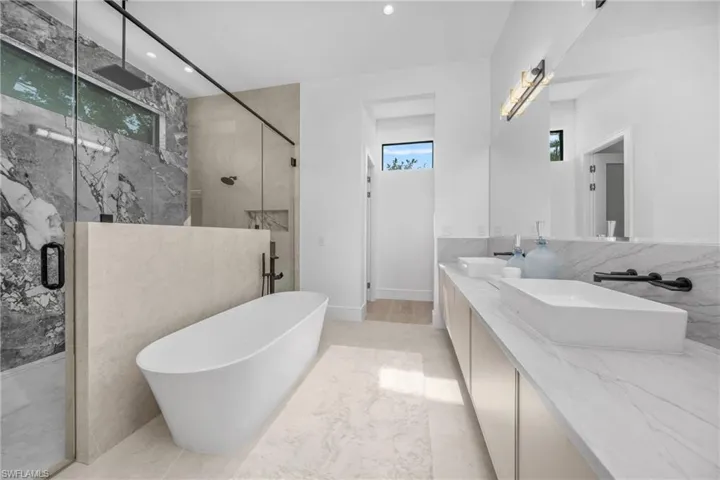 Full bath featuring recessed lighting, a sink, a freestanding bath, a marble finish shower, and double vanity