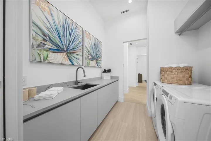 Clothes washing area with cabinet space, visible vents, independent washer and dryer, light wood-style floors, and a sink