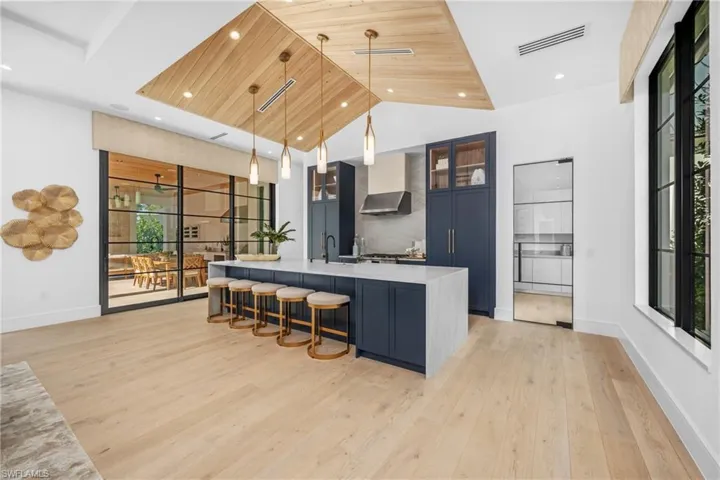 Kitchen with visible vents, hanging light fixtures, wall chimney range hood, light countertops, and glass insert cabinets