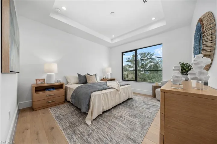 Bedroom featuring a raised ceiling, light wood-style flooring, and baseboards