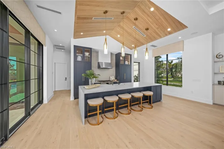 Kitchen featuring decorative light fixtures, visible vents, light wood-type flooring, wooden ceiling, and a large island with sink