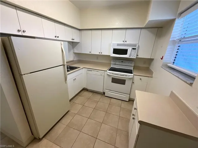 Kitchen featuring white appliances, white cabinets, light countertops, and light tile patterned floors