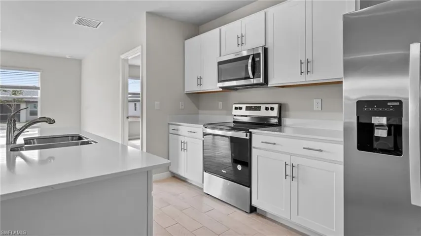 Kitchen featuring stainless steel appliances, white cabinetry, wood tiled floors, and light stone countertops