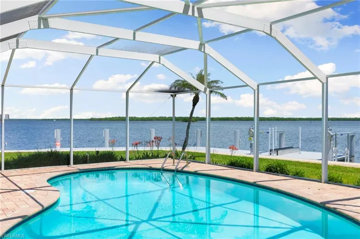 View of pool featuring glass enclosure, a water view, and a patio area
