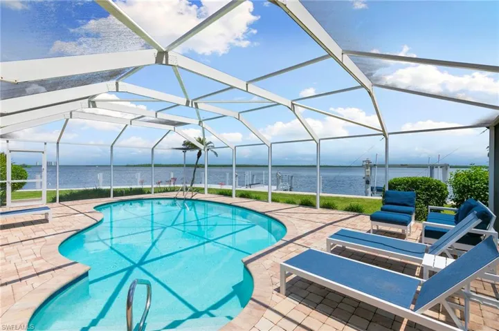 View of pool with glass enclosure, a patio area, and a water view