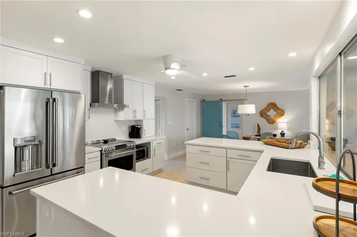 Kitchen with appliances with stainless steel finishes, sink, wall chimney exhaust hood, kitchen peninsula, and ceiling fan
