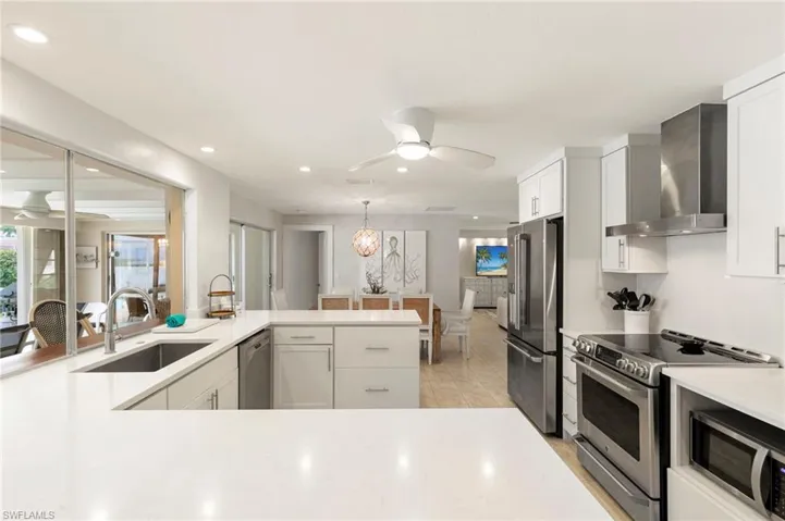 Kitchen featuring stainless steel appliances, kitchen peninsula, sink, ceiling fan, and wall chimney exhaust hood