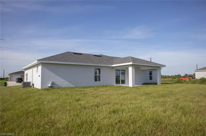 Rear view of house with stucco siding, a shingled roof, a lawn, and a patio