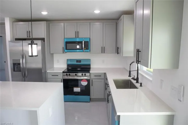 Kitchen with stainless steel appliances, gray cabinetry, light stone counters, light tile patterned floors, and recessed lighting