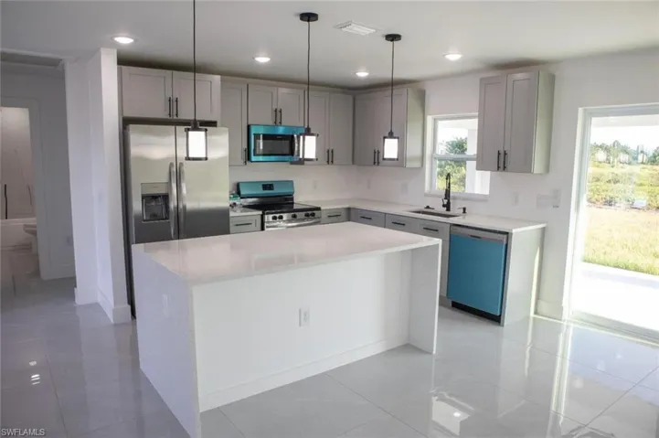 Kitchen featuring gray cabinetry, light tile patterned flooring, light stone counters, appliances with stainless steel finishes, and a kitchen island