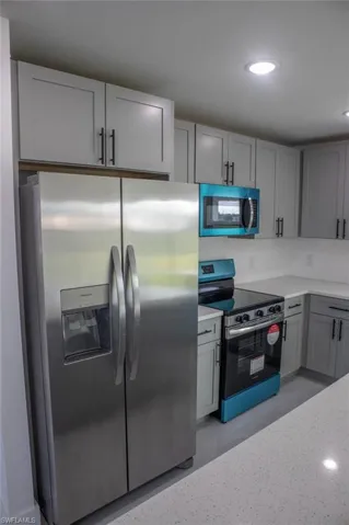Kitchen with appliances with stainless steel finishes, gray cabinetry, recessed lighting, and light stone countertops