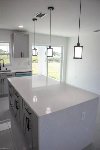 Kitchen featuring hanging light fixtures, gray cabinetry, a large island, light stone counters, and dishwasher