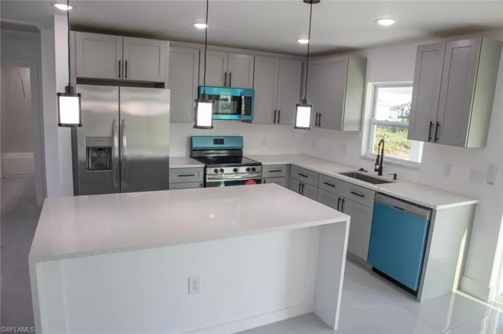 Kitchen with gray cabinets, appliances with stainless steel finishes, light stone countertops, light tile patterned floors, and a kitchen island