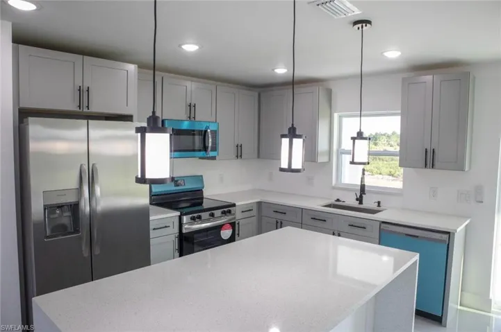 Kitchen featuring gray cabinets, stainless steel appliances, decorative light fixtures, light stone counters, and recessed lighting