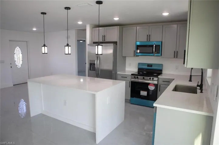 Kitchen with light stone counters, stainless steel appliances, hanging light fixtures, a kitchen island, and light tile patterned floors