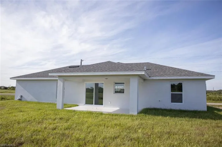 Rear view of house with stucco siding, roof with shingles, a yard, and a patio area