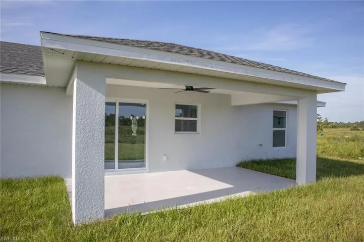 Back of house featuring a patio, stucco siding, a ceiling fan, a shingled roof, and a lawn