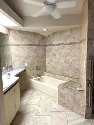 Bathroom with vanity, tile walls, a bathing tub, and ceiling fan