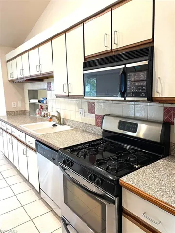 Kitchen with white cabinetry, sink, stainless steel appliances, lofted ceiling, and decorative backsplash