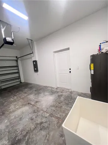 Garage featuring electric panel, a garage door opener, water heater, and a sink