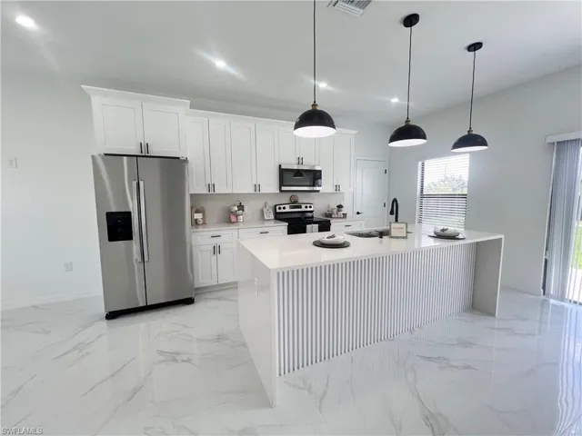 Kitchen featuring stainless steel appliances, a sink, light marble finish floors, a center island with sink, and white cabinetry