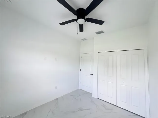 Unfurnished bedroom with light marble finish floors, lofted ceiling, a closet, baseboards, and a ceiling fan