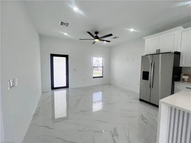 Kitchen with stainless steel refrigerator with ice dispenser, white cabinetry, baseboards, ceiling fan, and light marble finish flooring