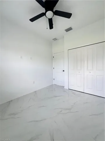 Unfurnished bedroom with marble look tiles, baseboards, a closet, and a ceiling fan