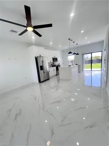 Unfurnished living room featuring recessed lighting, light marble finish flooring, a ceiling fan, baseboards, and a sink