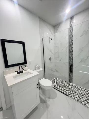 Bathroom featuring toilet, a marble finish shower, vanity, and marble finish floors