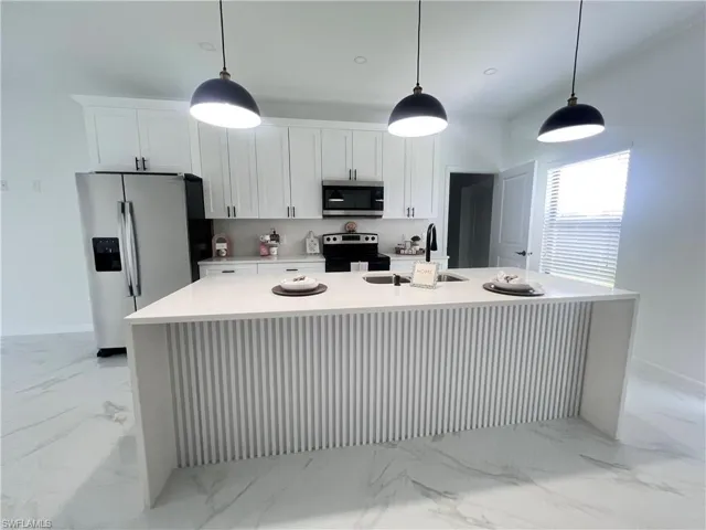 Kitchen with appliances with stainless steel finishes, a sink, light marble finish floors, white cabinetry, and a kitchen island with sink