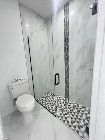 Full bathroom with marble finish floors, toilet, a marble finish shower, and baseboards